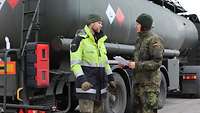 Eine Soldatin steht mit einem Schreibblock in der Hand mit einem weiteren Soldaten vor einem großen Tankfahrzeug.