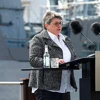 Eine Frau steht an einem Rednerpult mit zwei großen Mikrophonen.