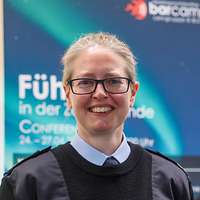 Oberfeldveterinär Dr. Britta W. blickt in die Kamera, hinter ihr ist ein Plakat des „BarCamps“