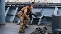 Zwei Soldaten an Oberdeck holen die armdicke Festmacherleine des Schiffes durch.