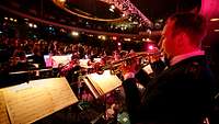 Ein Soldat spielt auf seiner Trompete zusammen mit der Big Band, die vor ihm sitzt.