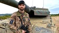 Ein bewaffneter Soldat steht vor seinem Panzer.