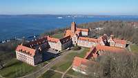 Mehrere Gebäude mit roten Dächern, im Hintergrund die Flensburger Förde