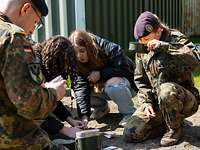 Mädchen des GirlsDay und Soldaten essen mit Kochgeschirr.