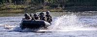 Bewaffnete Soldaten fahren mit einem Schlauchboot schnell über einen Fluss.