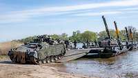 In der Sonne fährt ein Panzer von einer Fähre an das Ufer.
