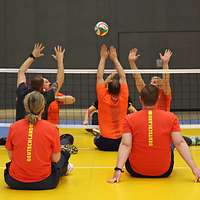Mehrere Sportler spielen Sitzvolleyball.