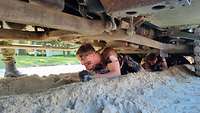 Ein junger Mann gleitet durch Sand unter einem Fahrzeug.