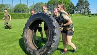 Bundeswehr Olympix 2023 Vier junge Frauen heben einen großen Reifen an, ihre Gesichter zeigen Anstrengung.
