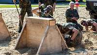 Bundeswehr Olympix 2023 Ein junger Mann gräbt sich mit den Händen unter einem Hindernis hindurch.