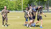 Bundeswehr Olympix 2023 Vier Männer tragen eine Puppe. Daneben ein Soldat, der sie anfeuert.