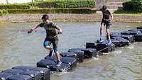 Bundeswehr Olympix 2023 Zwei Männer balancieren über Pontons im Wasser.