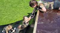 Bundeswehr Olympix 2023 Drei Frauen an einer Schrägwand, die Obere greift die Hand der Mittleren, eine hilft von unten.
