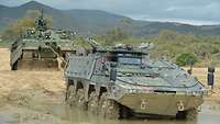 Ein schwerer Bergepanzer zieht einen Radpanzer aus einem mit Wasser gefüllten Schlammloch.