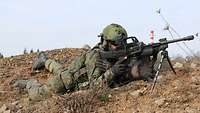 Ein Soldat liegt mit dem MG 4 im Anschlag auf dem Boden und schaut durch das Visier der Waffe. Er trägt Helm und Schutzweste.