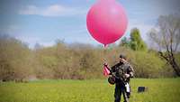 Ein Soldat steht mit einem Heliumballon, an der eine Messsonde befestigt ist, auf einer Wiese