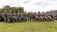 Vor zwei Gefechtsfahrzeugen auf einer Wiese stehen zahlreiche Soldaten und ein Zivilist.