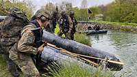 Mehrere Soldaten befinden sich am Ufer an einem Schlauchboot, um es im Kanal niederzulassen.
