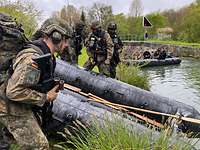 Mehrere Soldaten befinden sich am Ufer an einem Schlauchboot, um es im Kanal niederzulassen.