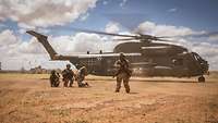 Soldaten stehen in der Wüste vor einem Transporthubschrauber CH-53 MedEvac und sichern die Umgebung.