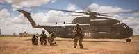 Soldaten stehen in der Wüste vor einem Transporthubschrauber CH-53 MedEvac und sichern die Umgebung.