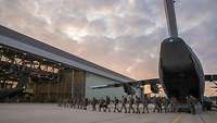 Mehrere Soldatinnen und Soldaten gehen aus einem militärischen Flugzeug in einen Hangar am Flughafen