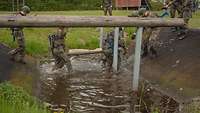 Mehrere Soldaten laufen mit einer Transporttrage durch einen Wassergraben.