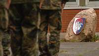 Mehrere Soldaten stehen auf einer Wiese und vor einem Stein mit einem Kompaniewappen.