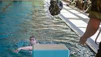 Ein Mann in einem Schwimmbecken wirft einen Kleidersack an den Beckenrand.