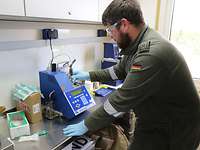 3N2A1514 Ein Soldat steht an einem Tisch mit einem Messgerät in einem Laborcontainer.