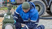 Ein Soldat kniet zur Kontrolle auf einem Schotterplatz neben einen Schieber einer Pipeline.