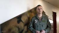 The squadron commander stands in front of a wall.