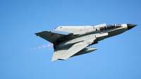 A combat aircraft flies past the photographer in a diagonal low-level flight.