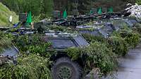 Mehrere getarnte Radpanzer stehen nebeneinander auf einer nassen, grauen Betonfläche.