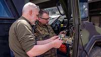 Zwei Soldaten stehen neben einer geöffneten Tür eines gepanzerten Fahrzeugs und reparieren sie.