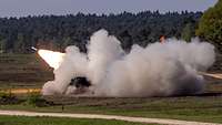 Ein Raketenwerfer feuert auf einem Feld eine Rakete und erzeugt dabei weißen Rauch und Feuer.