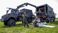 Mehrere Soldaten bergen eine weiße Drohne mit einem Lastwagen auf einer Wiese.