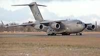 A grey military transport aircraft taking off at an airfield.