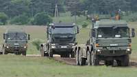 Drei LKW fahren hintereinander durch Gelände auf Feldwegen