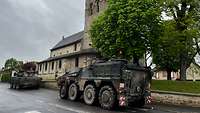 Zwei gepanzerte Fahrzeuge stehen auf einer Dorfstraße vor einer Kirche