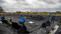 People in blue work clothes pull black foils through a basin