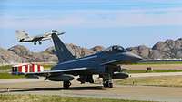 Jet takiing on an airfield while a second one in den Background is landing