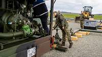 Ein Soldat arbeitet an einer mobilen Pumpstation, ein weiterer Soldat an dem Schieber der Pipeline.