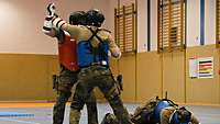 Soldaten in Uniform und Schutzausrüstung kämpfen mit Fäusten in einer Halle.