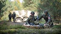 Eine Soldatin und ein Soldat vom Sanitätsdienst versorgen einen verletzten Kameraden im Gelände.