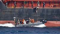 Ein Speedboat hält an der Schiffswand eines Handelsschiffes. Ein Soldat steigt auf der Lotsenleiter die Bordwand hinauf.
