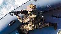 Ein Soldat mit einer Waffe in der Hand kniet auf einem Speedboat.