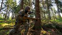 Zwei Soldaten laufen mit Gewehren im Anschlag durch den Wald.