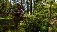 Ein Soldat mit Gewehr kniet im Wald. 