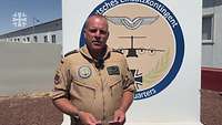 Ein Soldat steht in einem Camp vor einer Wand zu der Kamera gerichtet in einem Interview.
